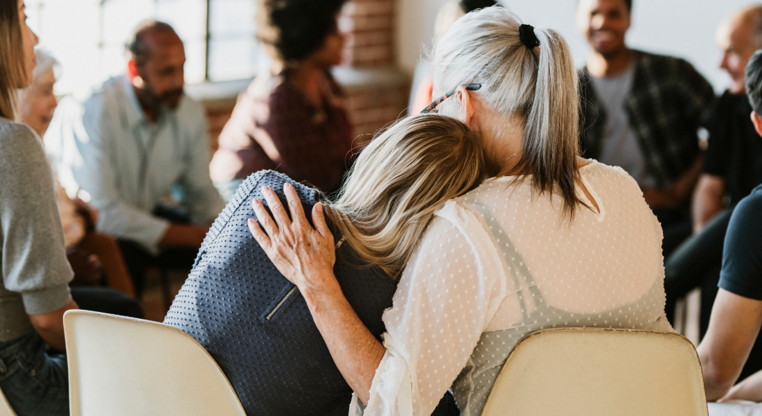 people sitting in a circle; one woman leans her head on another woman's shoulder. 