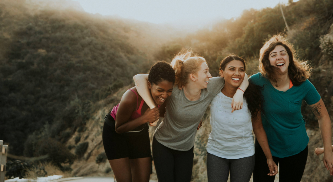 Four women arm in arm outside on a hike